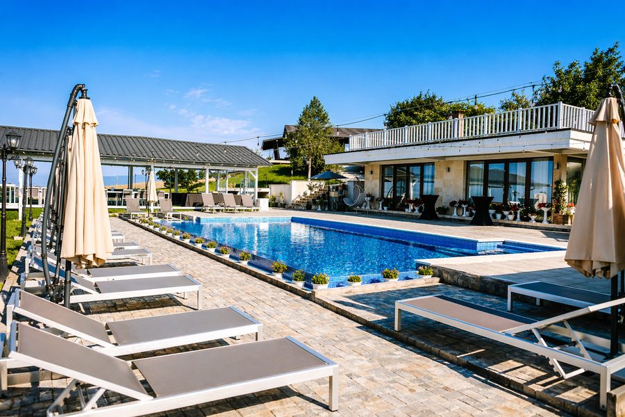 Piscina și clădirea cu terasă, văzute dinspre șezlonguri